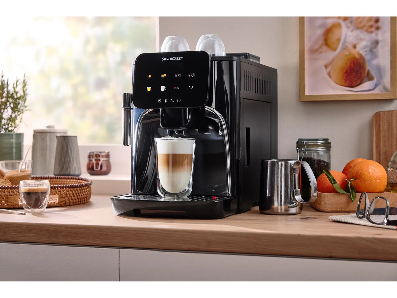 A SilverCrest coffee machine making a latte, with fruit and other kitchen items on a counter.