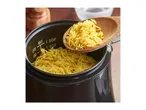 Cooked rice being scooped from a rice cooker with a wooden spoon.