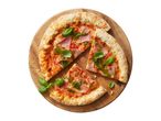 Pizza with ham, pesto, and basil on a wooden board, with two slices cut out.
