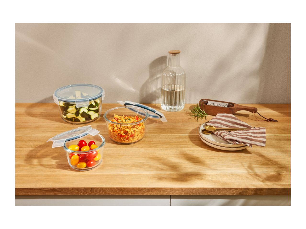 Glass food storage containers with fresh ingredients on a wooden counter.