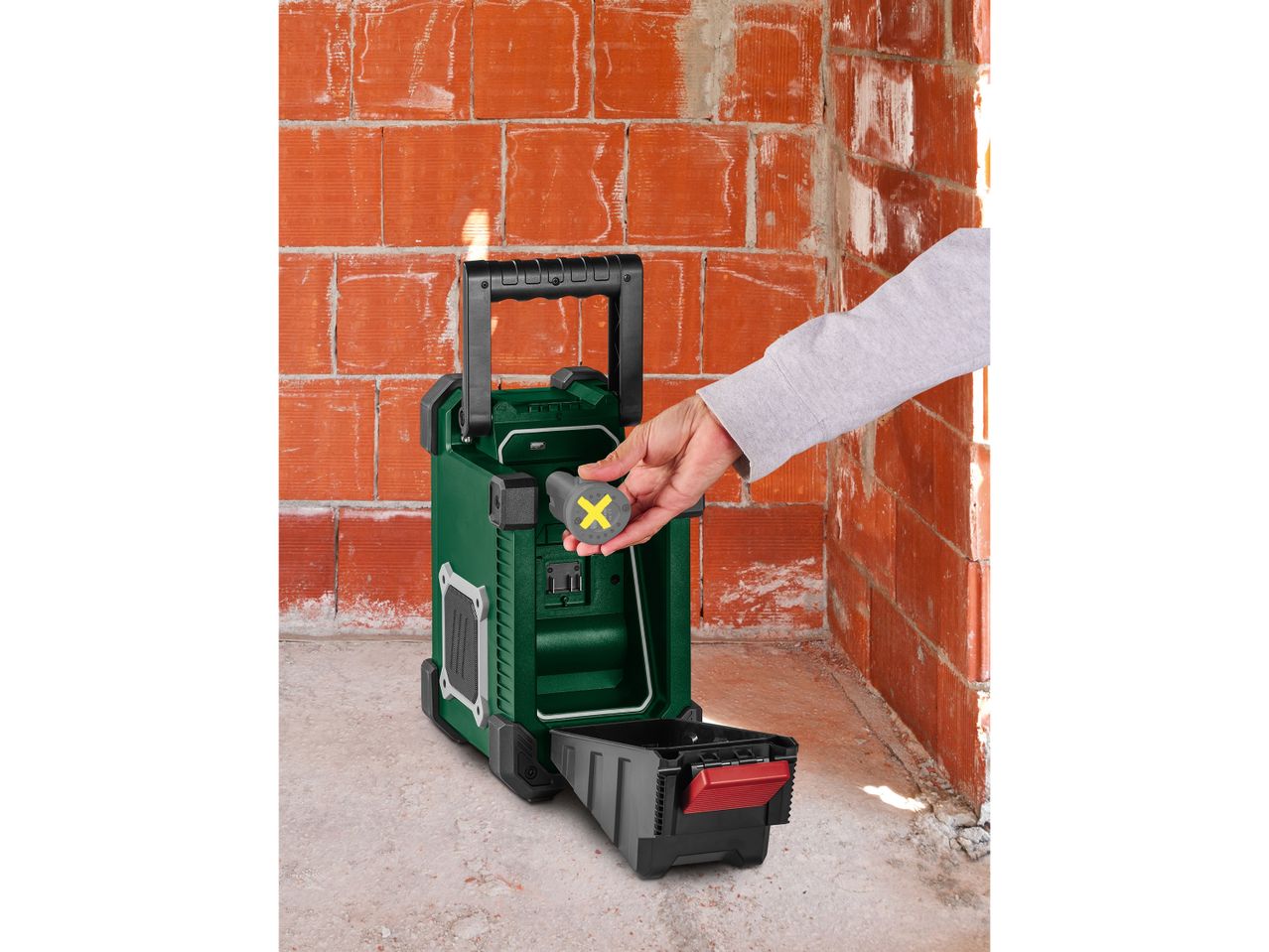 Person inserting a battery into a green portable radio on a construction site.