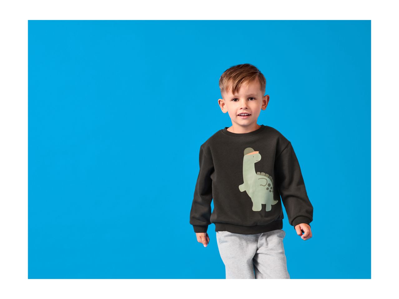 Smiling boy in a black dinosaur print sweatshirt and grey sweatpants.