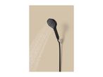 Black shower head spraying water, mounted on a beige wall.