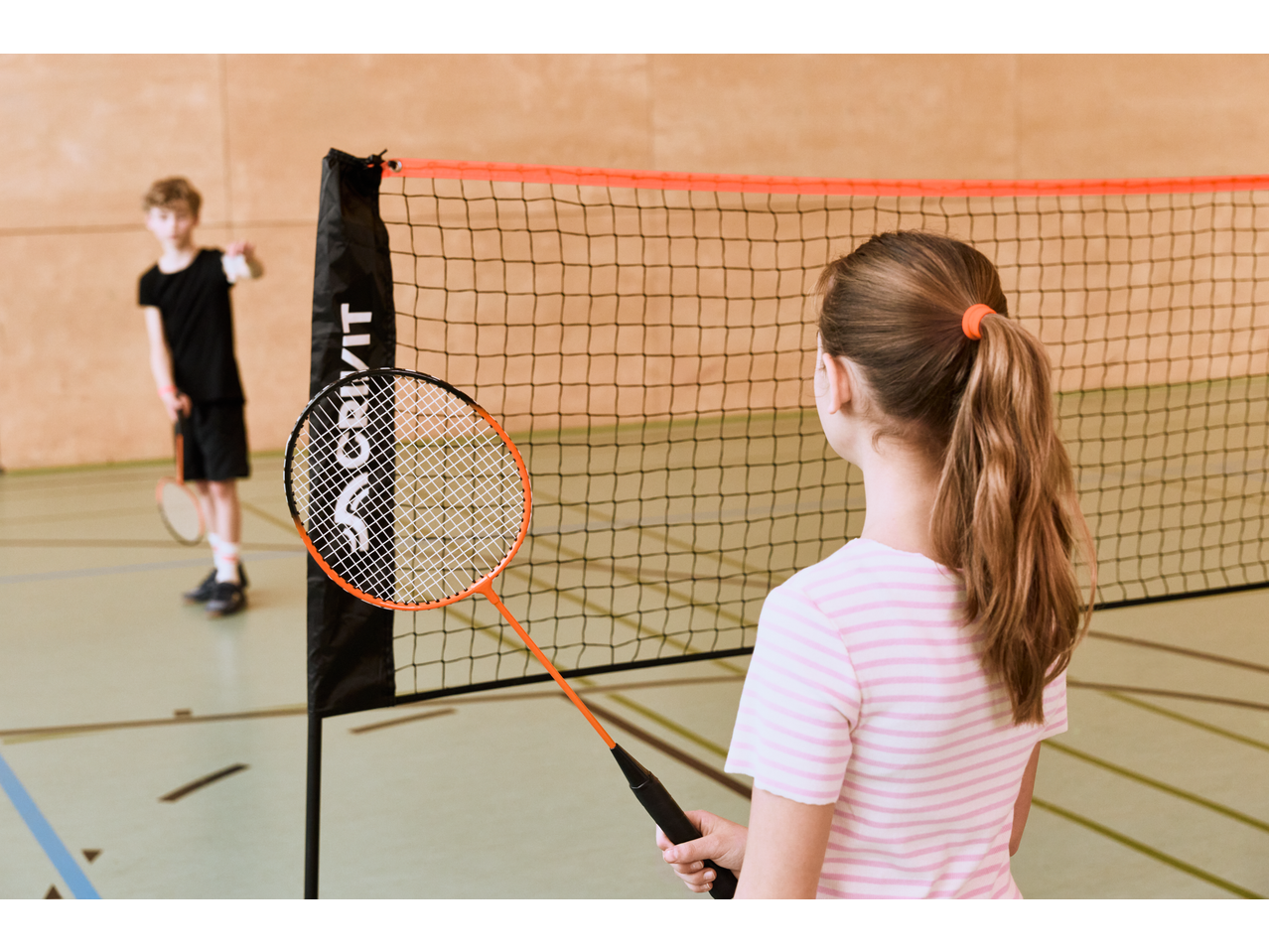 Conjunto de badminton CRIVIT com dois jogadores, rede e raquete em primeiro plano.
