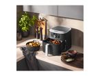 A black air fryer on a kitchen counter next to cooked food and sauces.