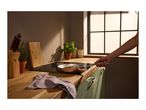 A person holding a copper frying pan on an induction hob in a kitchen.