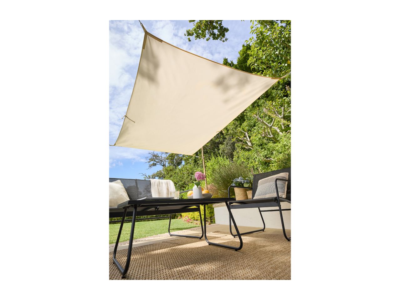 Outdoor patio with a beige sun shade, black metal garden furniture, and a woven rug.