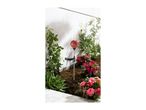 Solar garden light with a red mosaic globe in a garden bed with pink flowers.