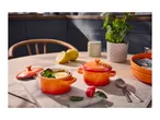 Orange mini casserole dishes with dessert, lemons, and raspberries on a kitchen table.