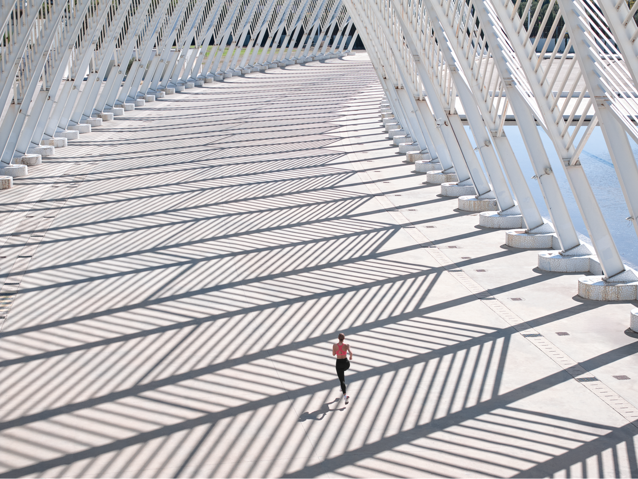 Mulher de leggings de corrida e sutiã desportivo a fazer jogging numa ponte moderna com sombras fortes.