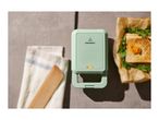 A light green SilverCrest sandwich maker with an illuminated indicator light, next to a sandwich.