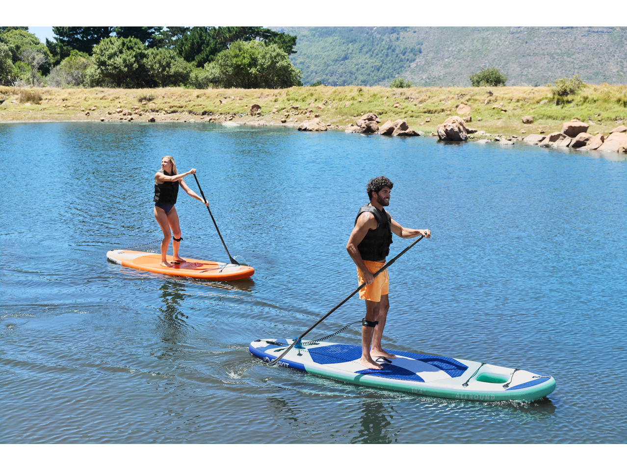 Two people paddleboarding on a lake with CRIVIT SUP boards and paddles.