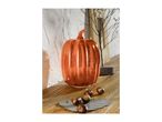 A shiny orange pumpkin decoration on a wooden surface with chestnuts.