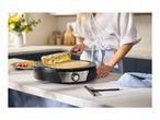A person making crepes on a crepe maker, with a plate of crepes and raspberries nearby.