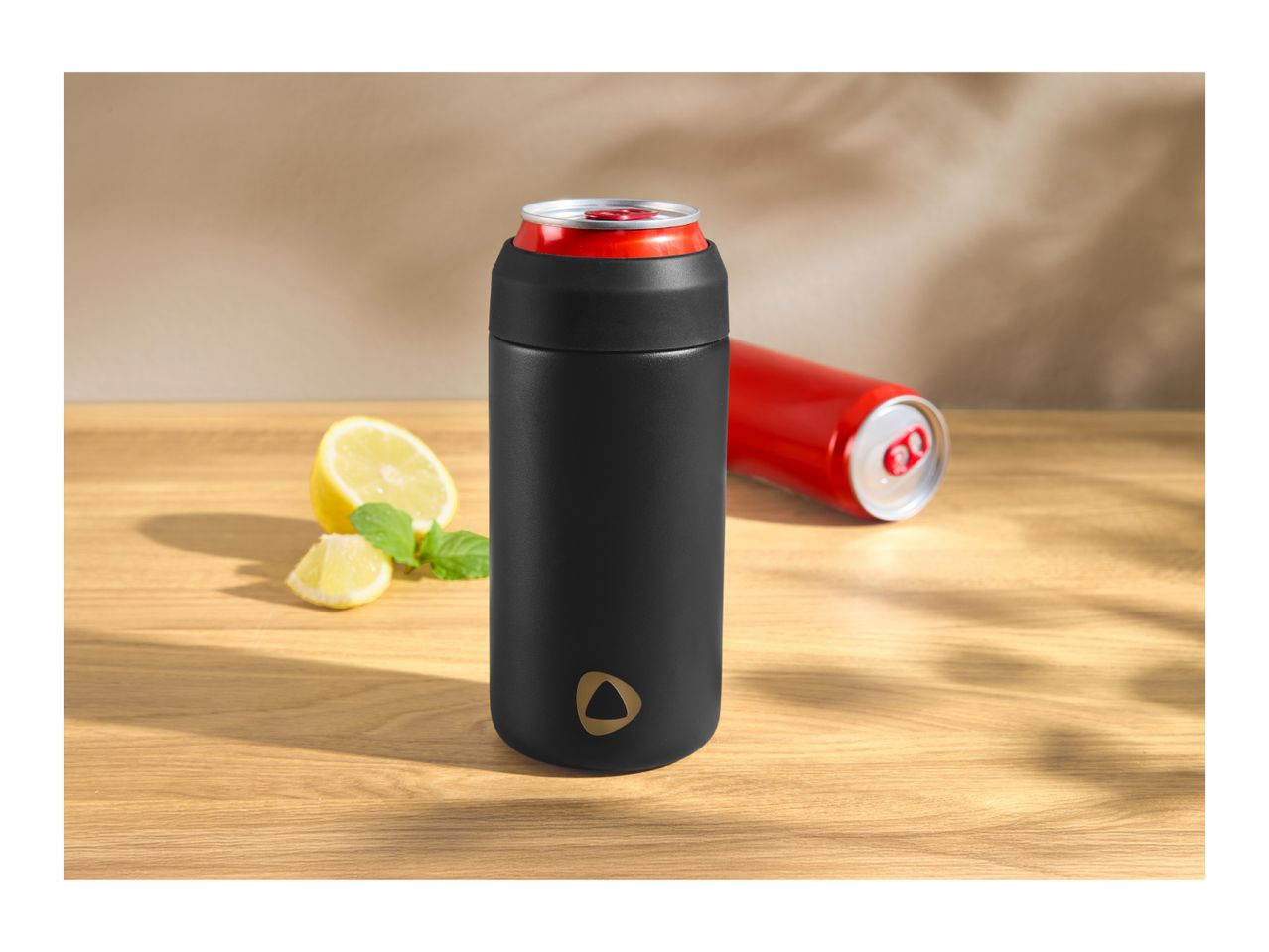Black insulated can cooler with a red soda can, lemon slices, and mint on a wooden table.
