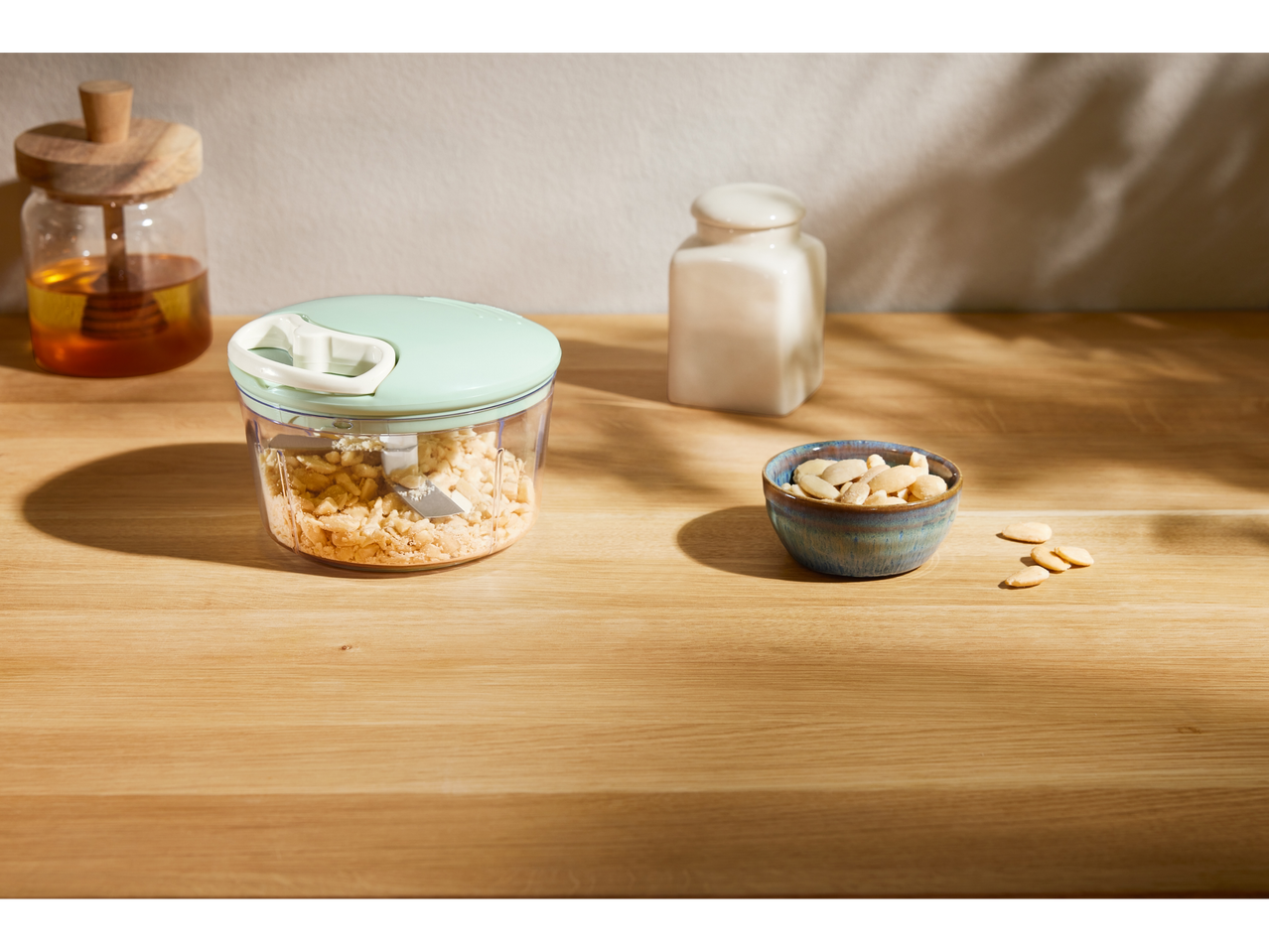 Ръчен кухненски чопър с нарязани бадеми на дървена маса.