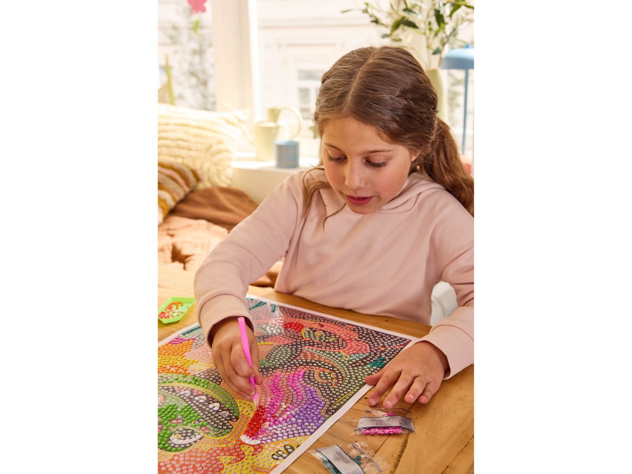 A girl doing diamond painting on a wooden table.
