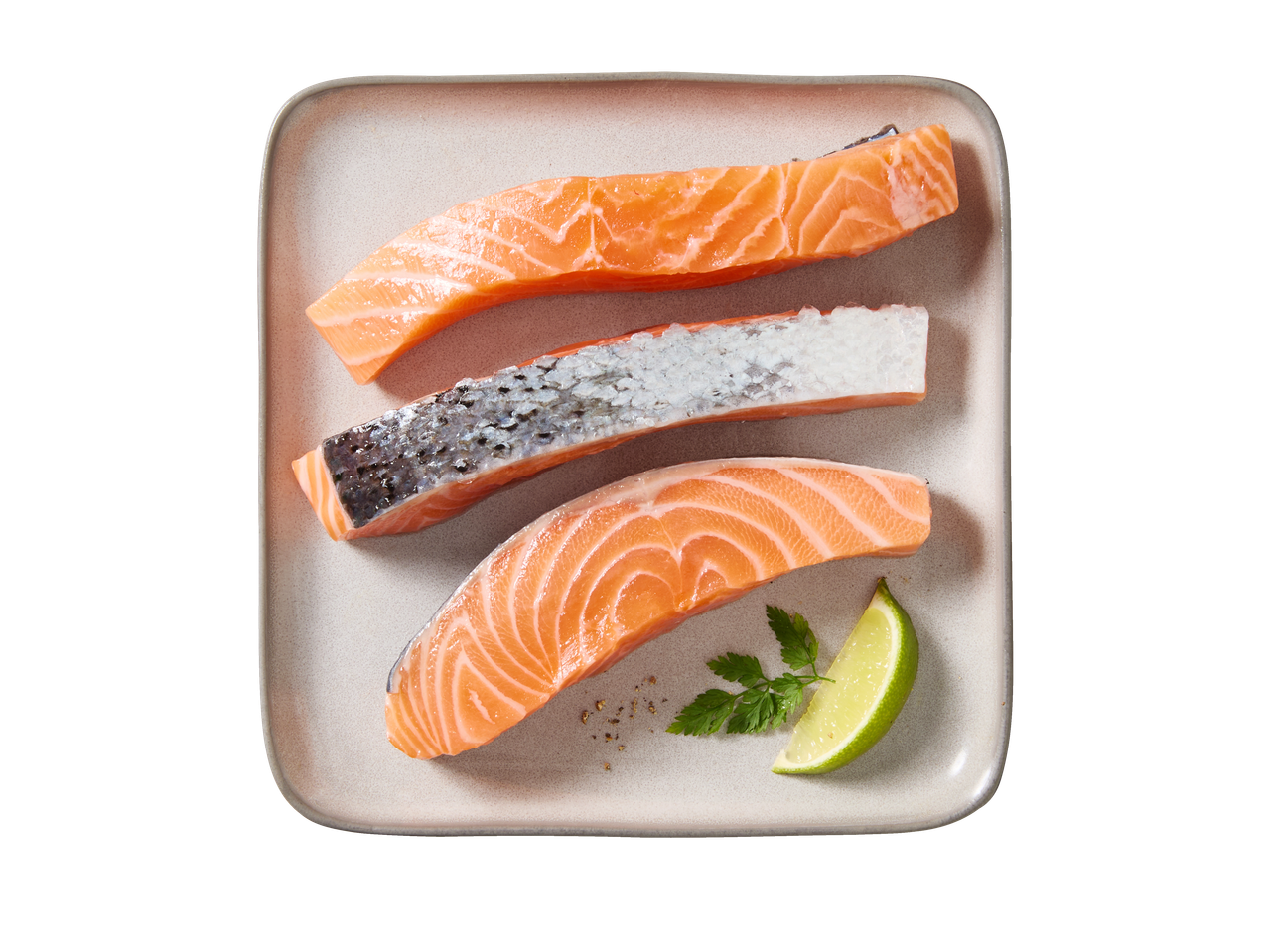 Trys žalios lašišos filė, viena su oda, lėkštėje su laimu ir petražolėmis.