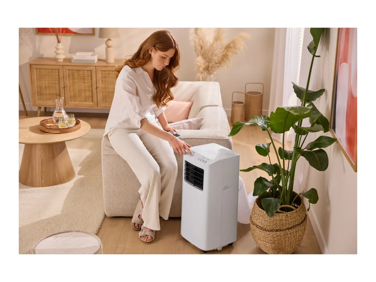 Woman adjusting a portable air conditioner in a cozy living room with natural decor.