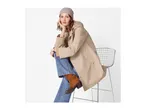 Woman in a beige raincoat, blue jeans, and brown boots, sitting on a chair.
