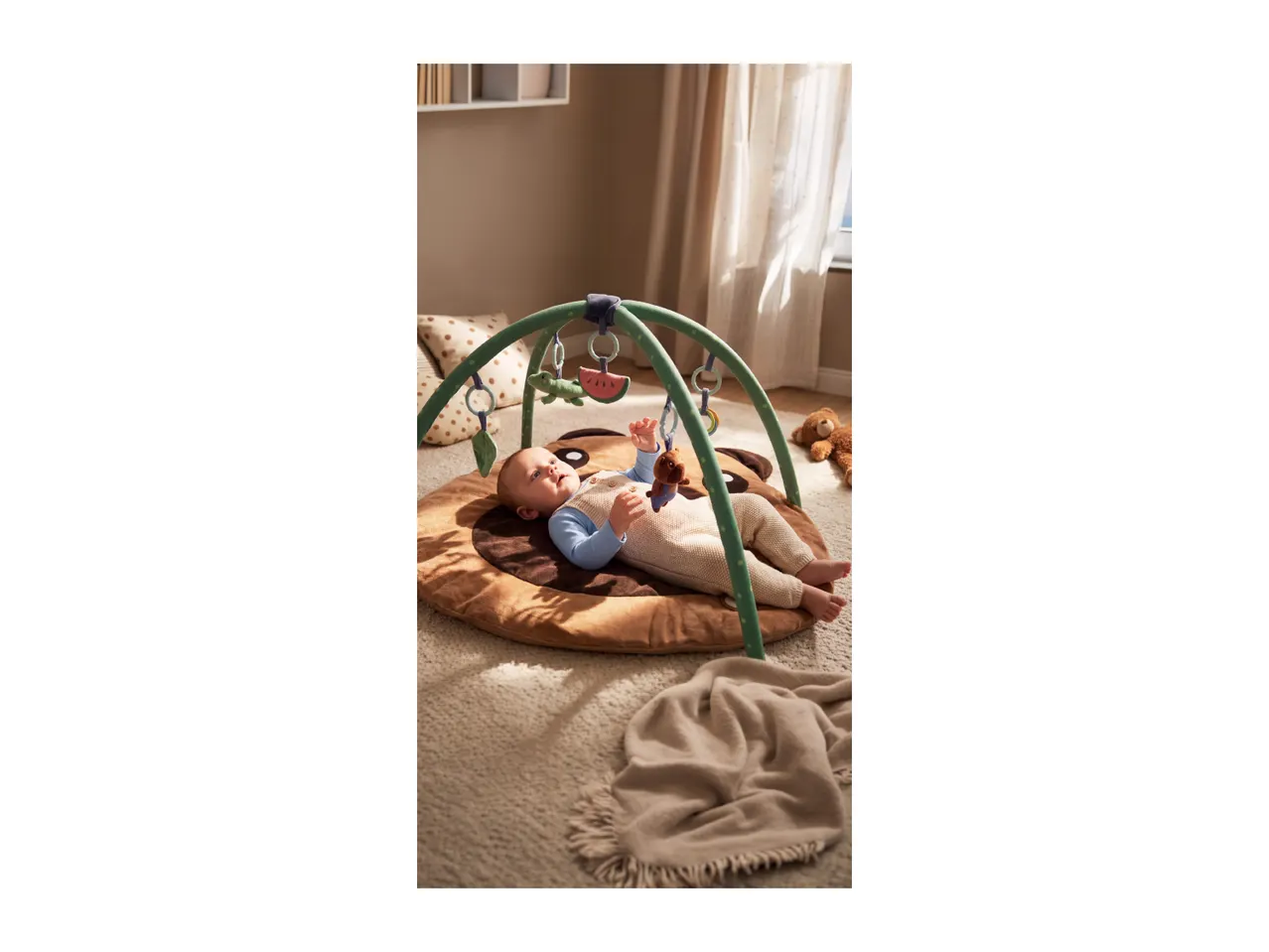 Baby lying on a brown playmat with a green activity arch and hanging toys.