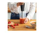Person blending tomato soup with an immersion blender, with fresh tomatoes nearby.