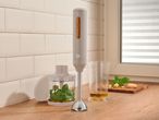 Hand blender with accessories, basil, parmesan, and olive oil on a kitchen counter.