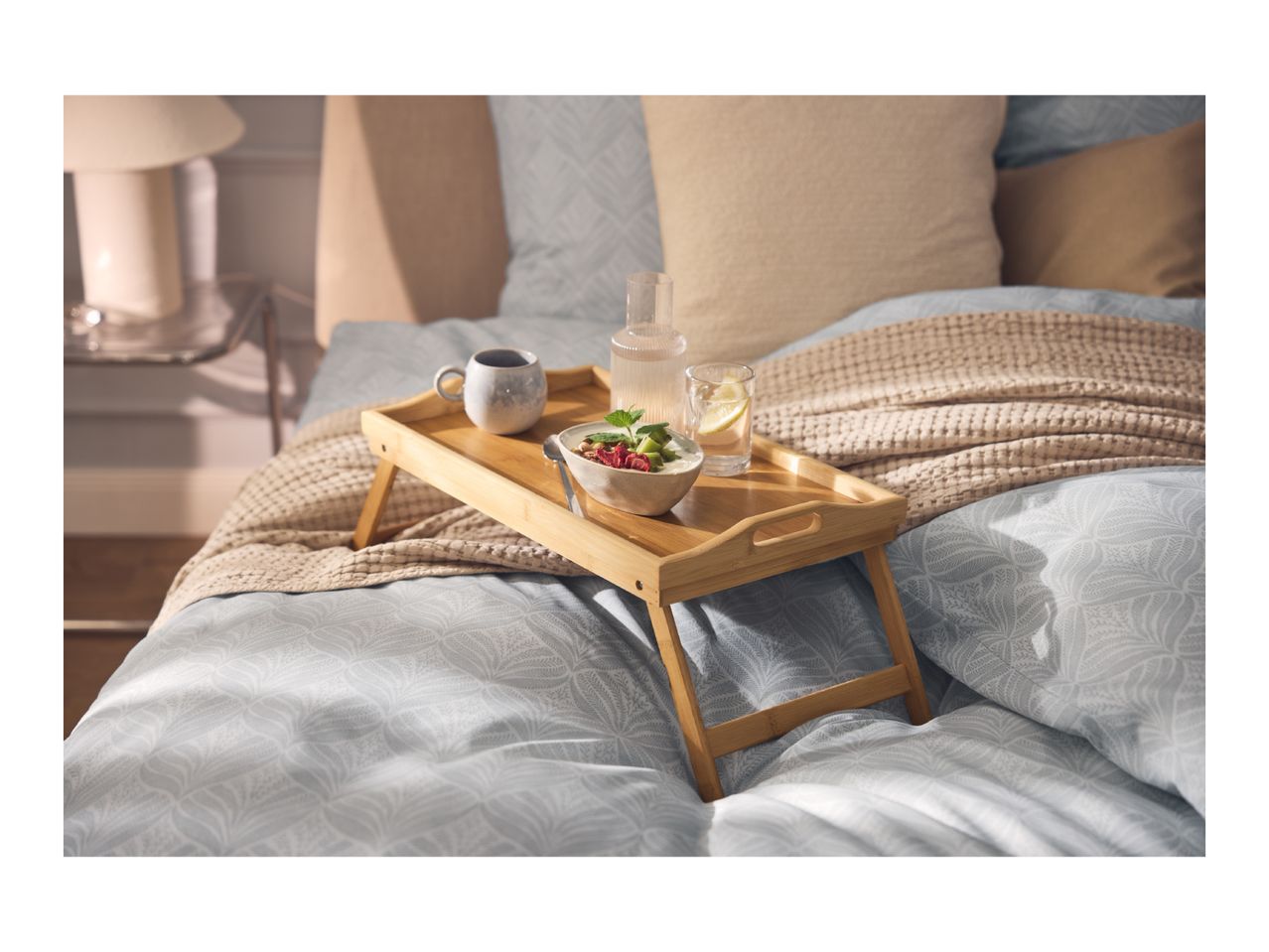 Breakfast in bed with a wooden tray holding a bowl of yogurt, fruit, a mug, and water.