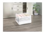 White fabric storage bin with a clear top, filled with clothes, on a wooden floor in front of a white cabinet.