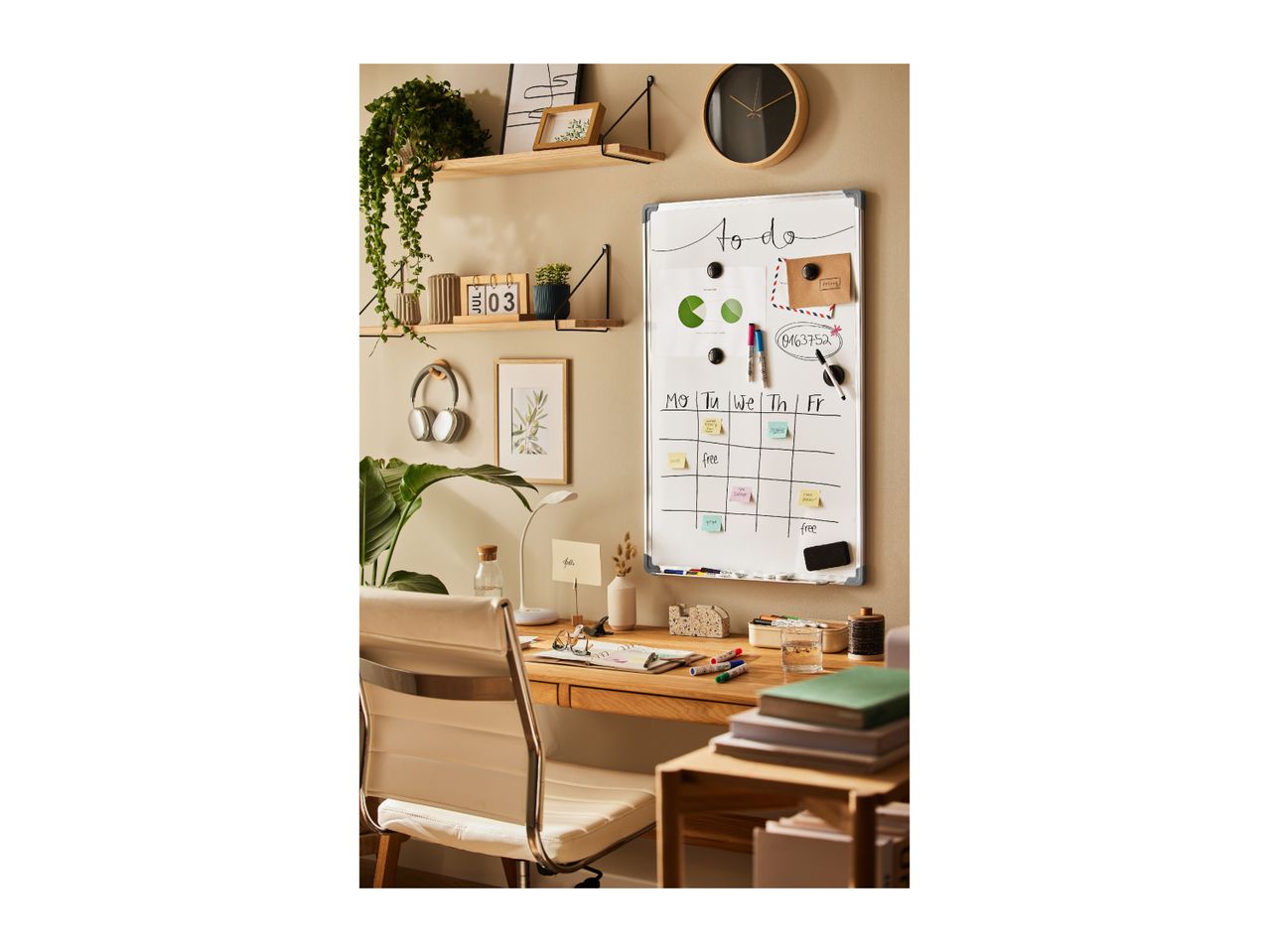 Home office with a whiteboard calendar, desk, and shelves with plants and decor.