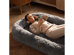 Woman relaxing on a grey Silentnight pet bed, wearing headphones and holding a phone.