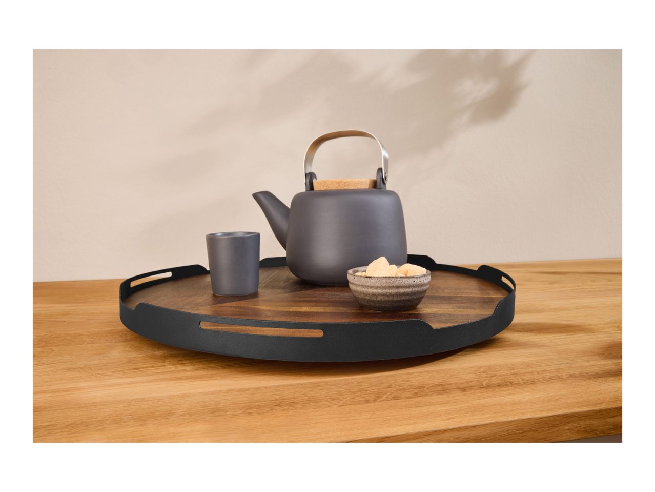 A dark grey teapot, a matching cup, and a small bowl of sugar cubes on a wooden serving tray.