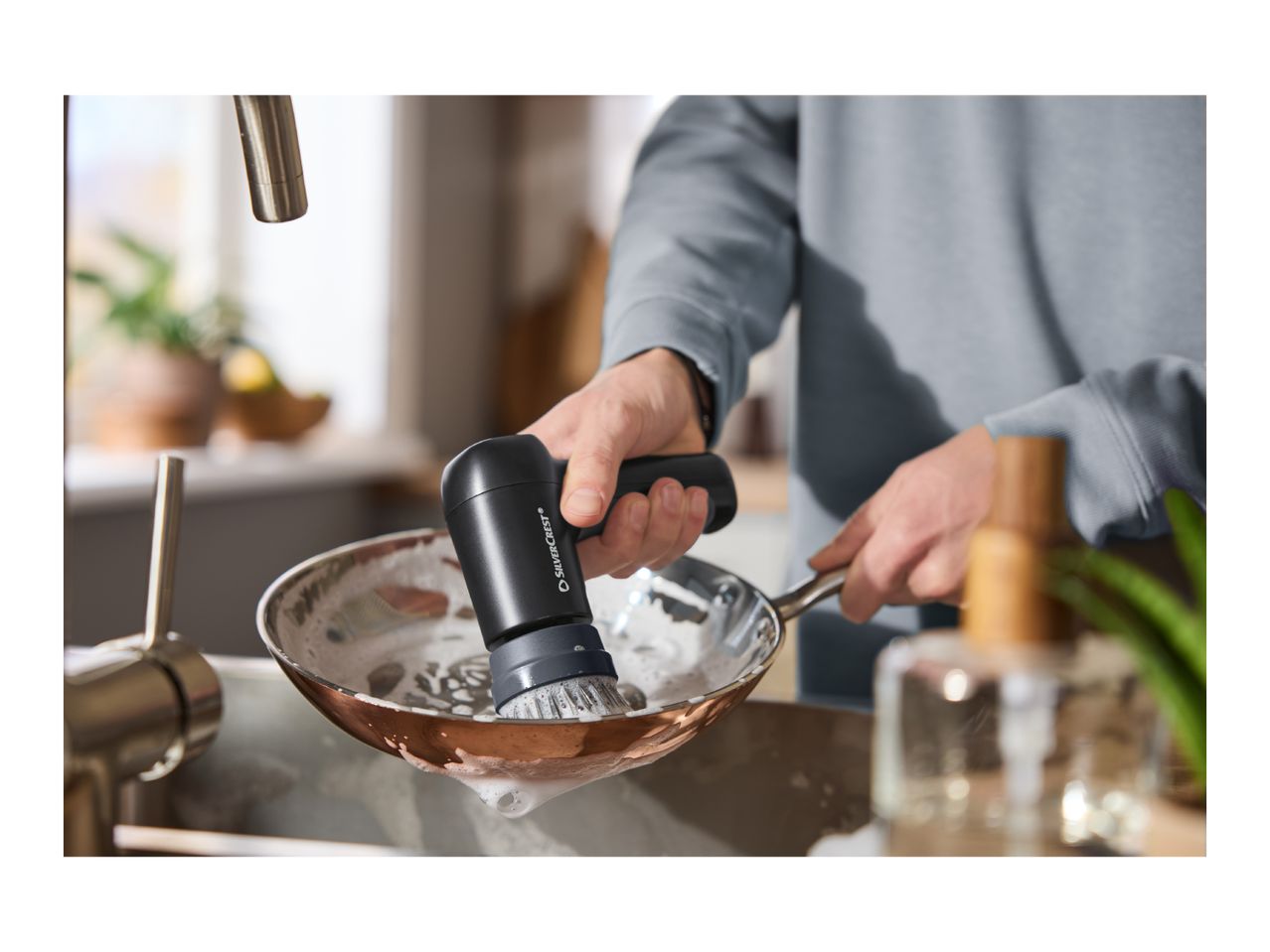 Person washing a pan with a dish brush in a kitchen sink.