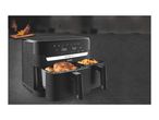 Black dual air fryer with cooked chicken and fries, with a person chopping food in the background.