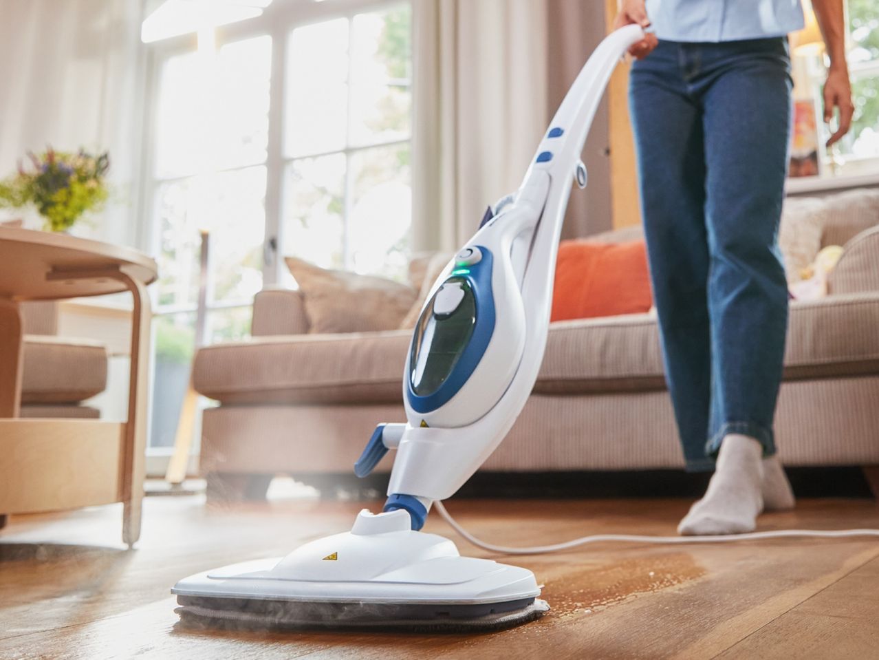 A person uses a steam mop to clean a hardwood floor.