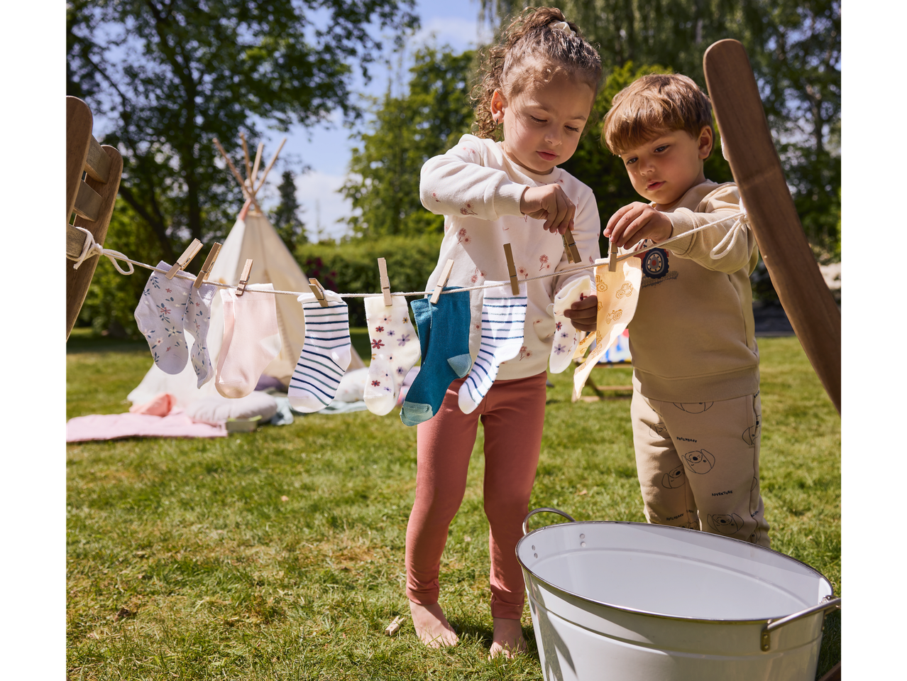 Crianças pendurando meias em um varal de brinquedo ao ar livre.