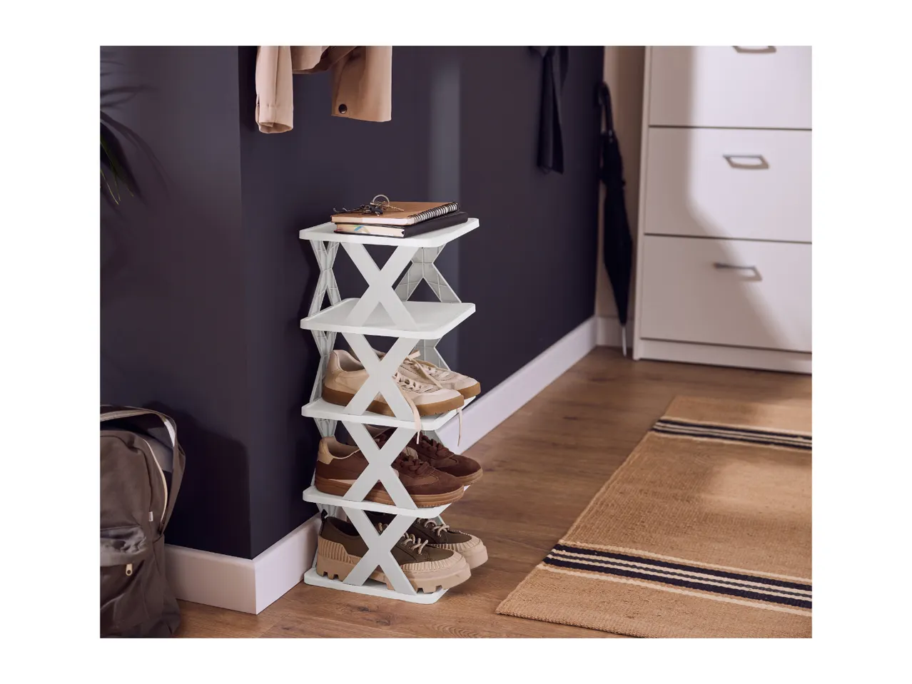 White foldable shoe rack with shoes, notebooks, and keys in an entryway.