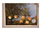 Halloween pumpkin string lights hanging in a window with autumn trees outside.