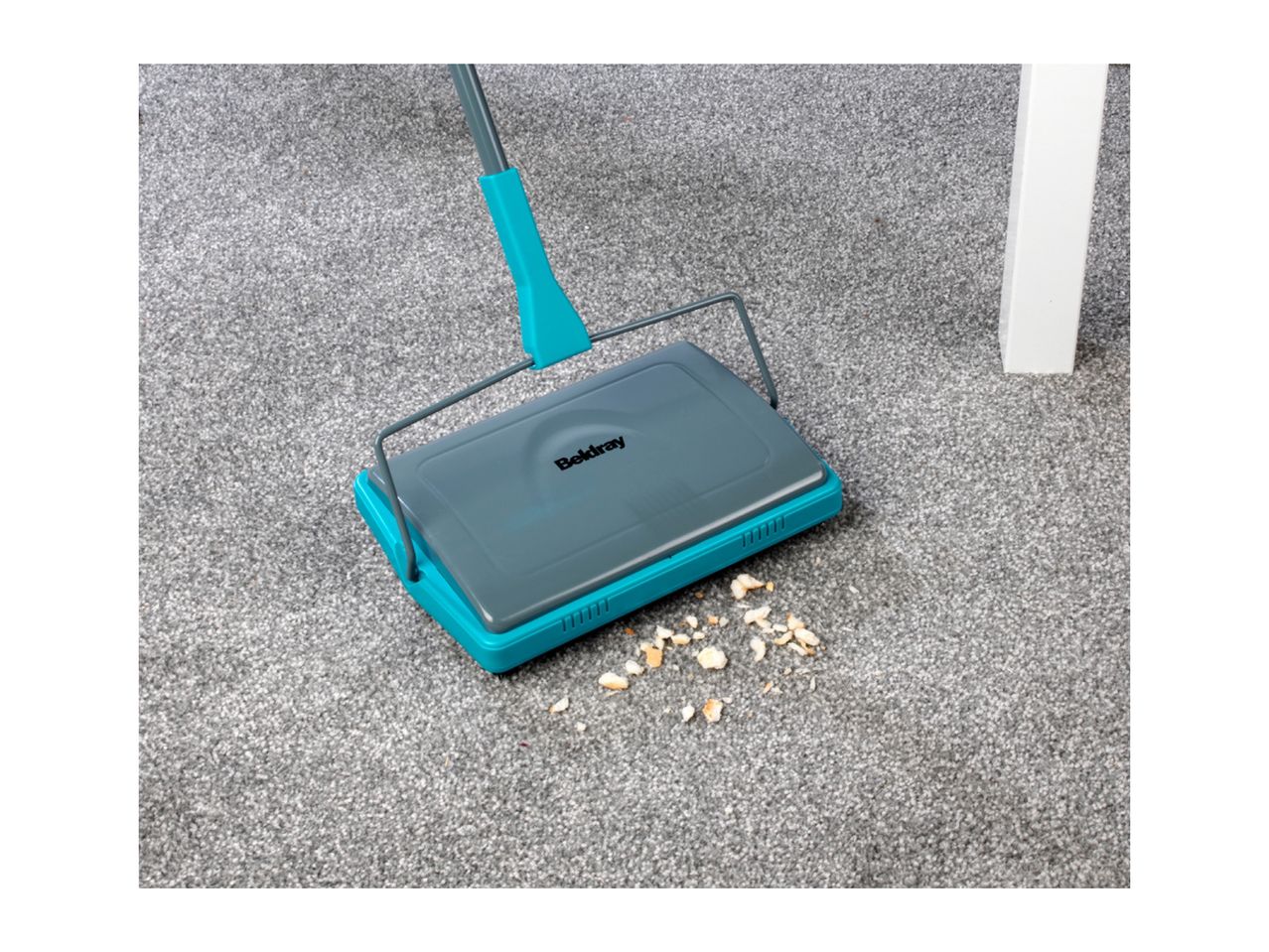 A Belray carpet sweeper cleans up crumbs on a grey carpet.