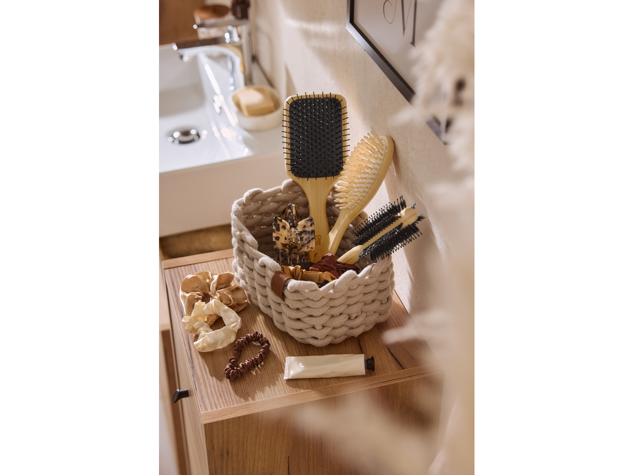 Perii de păr CIEN BEAUTY și accesorii într-un coș împletit, pe un dulap de baie din lemn.