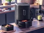 Black air fryer with food inside, digital display showing 180 degrees, and a spiralizer with zucchini noodles on a kitchen counter.