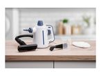 White and blue handheld steam cleaner with accessories on a wooden countertop.