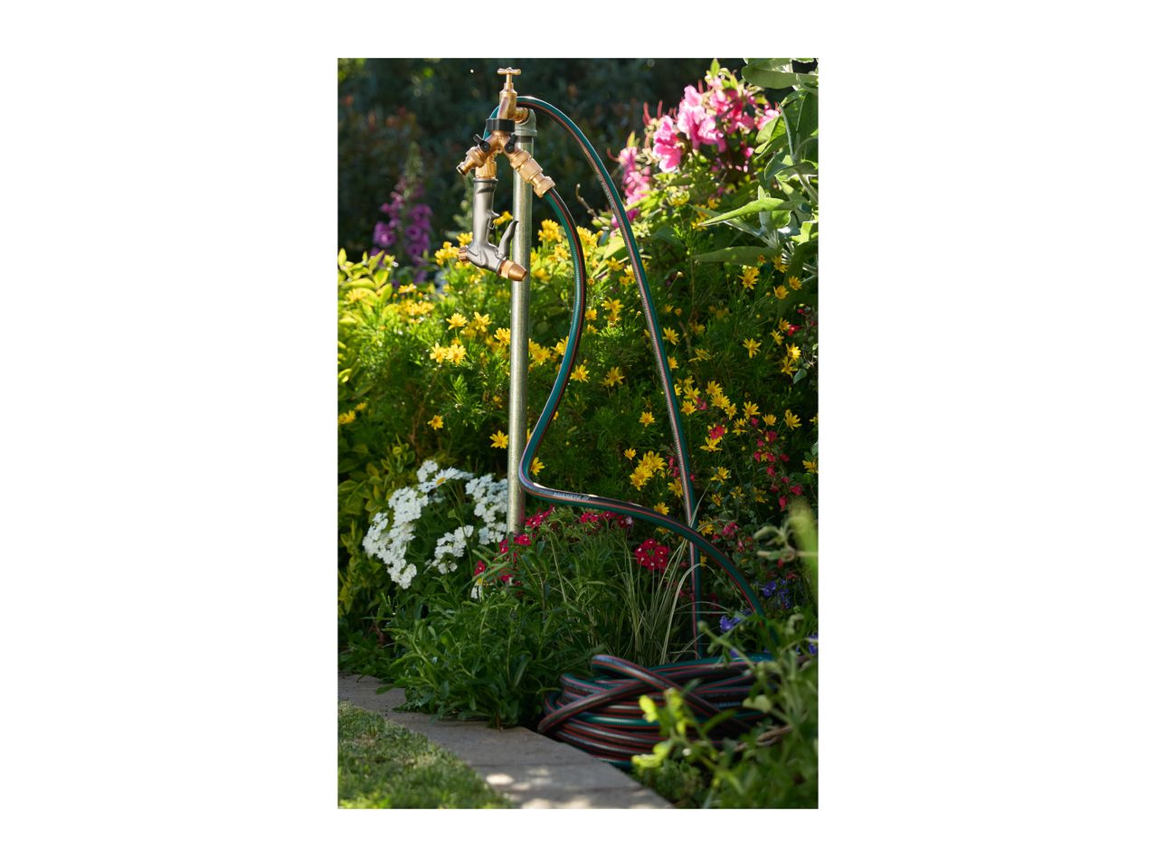 Garden hose and spray gun attached to an outdoor tap, surrounded by colorful flowers.