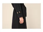 A person wearing a black coat with decorative buttons on the sleeve and a gold ring.