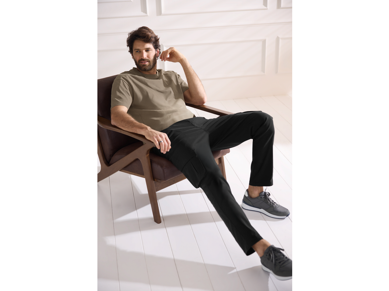 Bărbat în tricou ESMARA MEN și pantaloni negri, așezat într-un fotoliu.