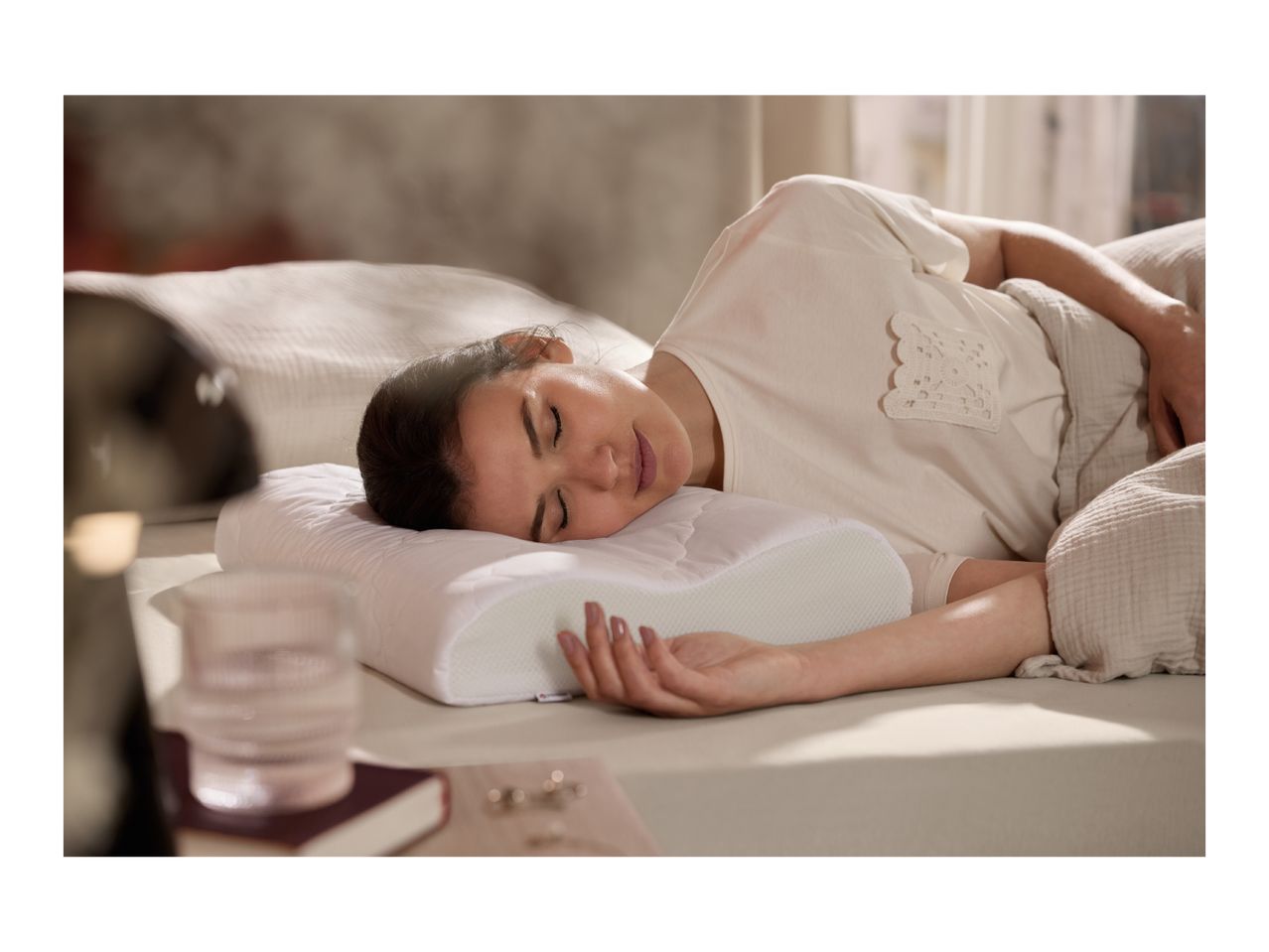 Woman sleeping peacefully on a contoured memory foam pillow in a bedroom.