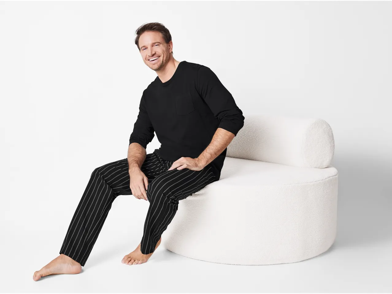 Lachende man in zwart gestreepte pyjama, zittend op een witte bank.