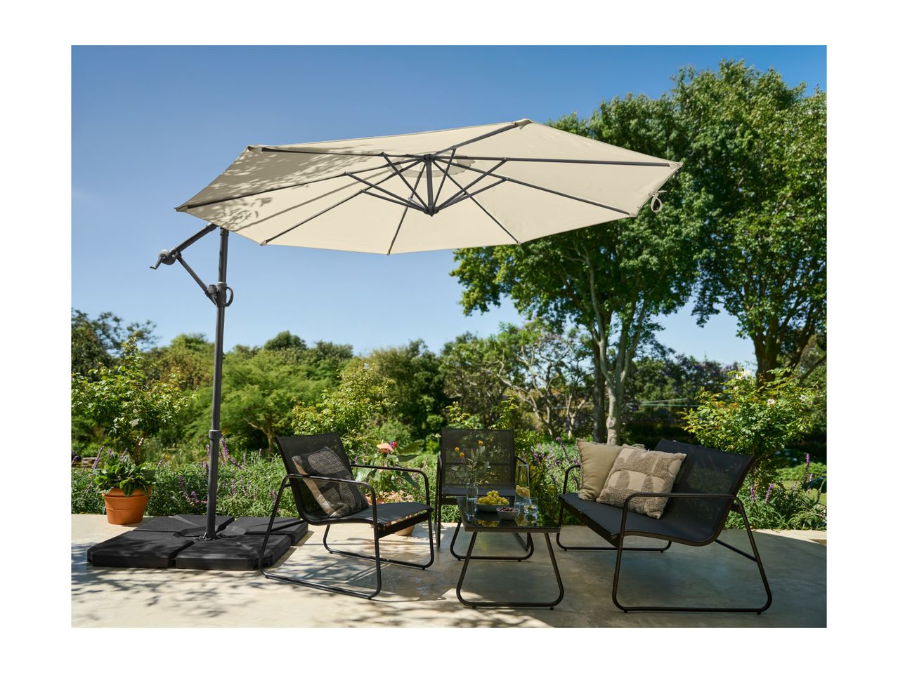Patio umbrella, two chairs, and a small table on a patio with lush greenery.