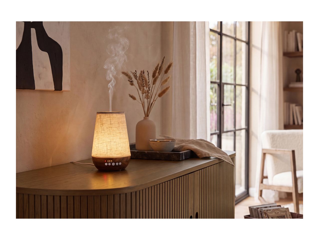 An elegant, glowing essential oil diffuser emitting mist on a wooden sideboard.