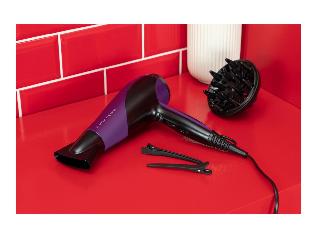 Hair dryer with diffuser and hair clips on a red surface with red tiled wall.